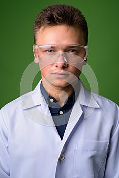 Young handsome man doctor wearing protective glasses against gre