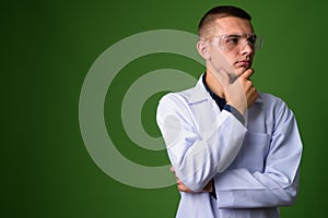 Young handsome man doctor wearing protective glasses against gre