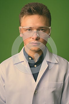 Young handsome man doctor wearing protective glasses against green background