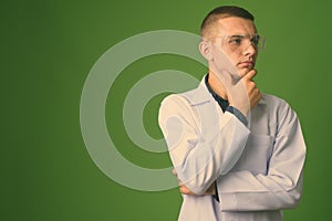 Young handsome man doctor wearing protective glasses against green background