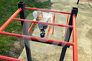 Young handsome man doing dips outside on parallel bars seen through the horizontal ladder