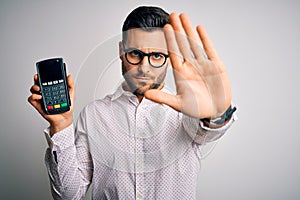 Young handsome man doing payment using dataphone over isolated white background with open hand doing stop sign with serious and