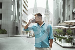 Young handsome man drinking coffee on the go walking down the street downtown feeling happy