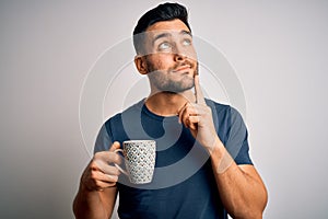 Young handsome man drinking a cup of hot coffee over white isolated background serious face thinking about question, very confused