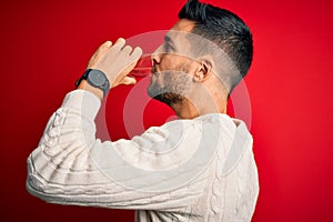 Young handsome man drinking glass of healthy water to refreshment standing over isolated red background