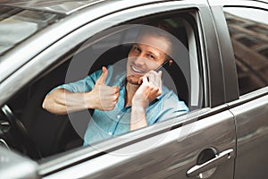 Young handsome man drives unsafely having conversation on his smartphone on the run showing like sign photo