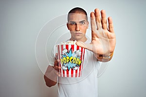 Young handsome man eating popcorn over white isolated background with open hand doing stop sign with serious and confident