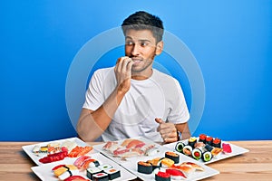 Young handsome man eating sushi sitting on the table looking stressed and nervous with hands on mouth biting nails