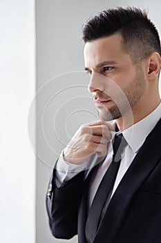 Young handsome man in elegant suit adjust his necktie