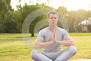 Young handsome man with eyes closed meditating at the park