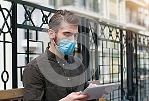 Young handsome man in face mask works intently with tablet computer