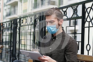 Young handsome man in face mask works intently with tablet computer