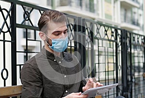 Young handsome man in face mask works intently with tablet computer