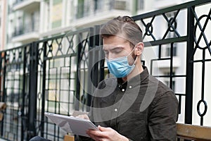 Young handsome man in face mask works with tablet computer