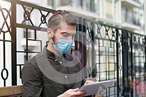 Young handsome man in face mask works with tablet computer
