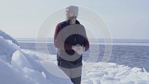 Young handsome man geologist focused on something near cold ice snowing glacier behind the winter sea. Slow motion