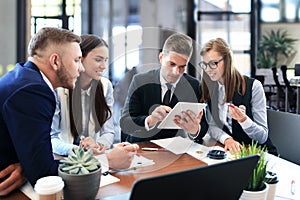 Young handsome man gesturing and discussing something while his coworkers listening to him sitting at the office table