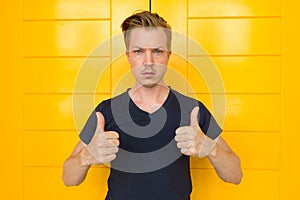 Young handsome man giving thumbs up in front of yellow door