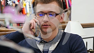 Young handsome man in glasses talking on the cellphone in shopping mall and working with laptop. Close-up