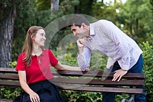 Young handsome man greeting his beloved partner who is sitting on a bench in the park