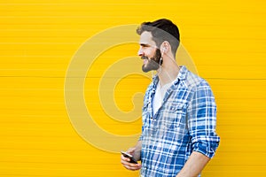 Young handsome man with headphones on yellow wall