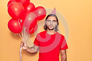 Young handsome man holding balloons thinking attitude and sober expression looking self confident