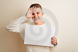 Young handsome man holding banner standing over isolated white background with happy face smiling doing ok sign with hand on eye