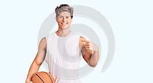 Young handsome man holding basketball ball pointing finger to one self smiling happy and proud