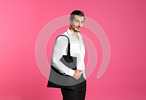 Young handsome man holding black tote bag on pink background, space for