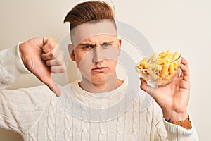 Young handsome man holding bowl with dry pasta standing over isolated white background with angry face, negative sign showing
