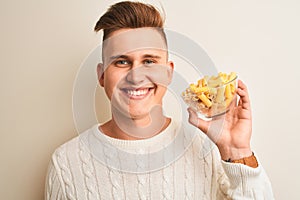 Young handsome man holding bowl with dry pasta standing over isolated white background with a happy face standing and smiling with