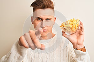 Young handsome man holding bowl with dry pasta standing over isolated white background pointing with finger to the camera and to