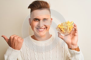 Young handsome man holding bowl with dry pasta standing over isolated white background pointing and showing with thumb up to the