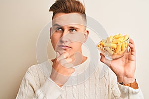 Young handsome man holding bowl with dry pasta standing over isolated white background serious face thinking about question, very