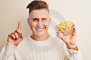 Young handsome man holding bowl with dry pasta standing over isolated white background surprised with an idea or question pointing