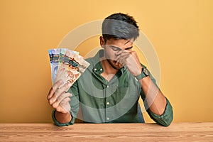 Young handsome man holding canadian dollars tired rubbing nose and eyes feeling fatigue and headache