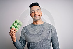 Young handsome man holding carton box of healthy fresh eggs over white background with a happy face standing and smiling with a