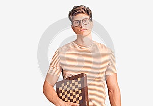 Young handsome man holding chess thinking attitude and sober expression looking self confident