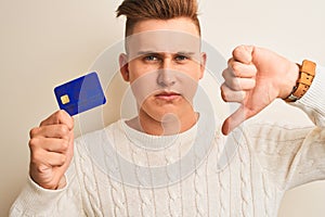 Young handsome man holding credit card over isolated white background with angry face, negative sign showing dislike with thumbs