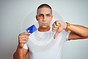 Young handsome man holding credit card over white isolated background with angry face, negative sign showing dislike with thumbs