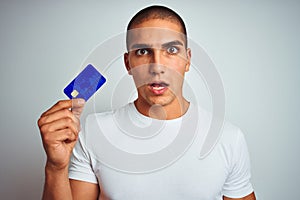 Young handsome man holding credit card over white isolated background scared in shock with a surprise face, afraid and excited
