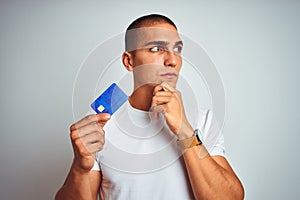 Young handsome man holding credit card over white isolated background serious face thinking about question, very confused idea