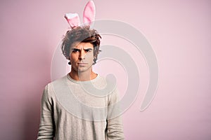 Young handsome man holding easter rabbit ears standing over isolated pink background skeptic and nervous, frowning upset because
