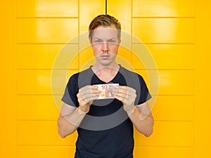 Young handsome man holding 10 euro in front of yellow door