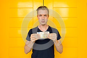 Young handsome man holding 50 euro in front of yellow door