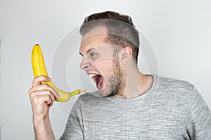 Young handsome man holding fresh banana like a smartphone screaming on isolated white background