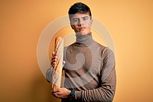 Young handsome man holding homemade fresh bread over isolated yellow background with a confident expression on smart face thinking