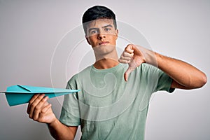 Young handsome man holding paper airplane over isolated white background with angry face, negative sign showing dislike with