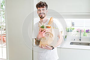 Young handsome man holding a paper bag full of fresh groceries at home