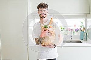 Young handsome man holding a paper bag full of fresh groceries at home